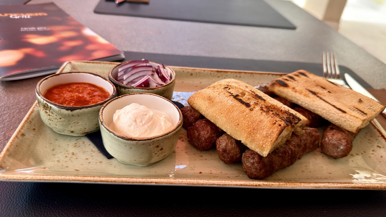 A plate of ćevapi with grilled bread, ajvar, onions and cream