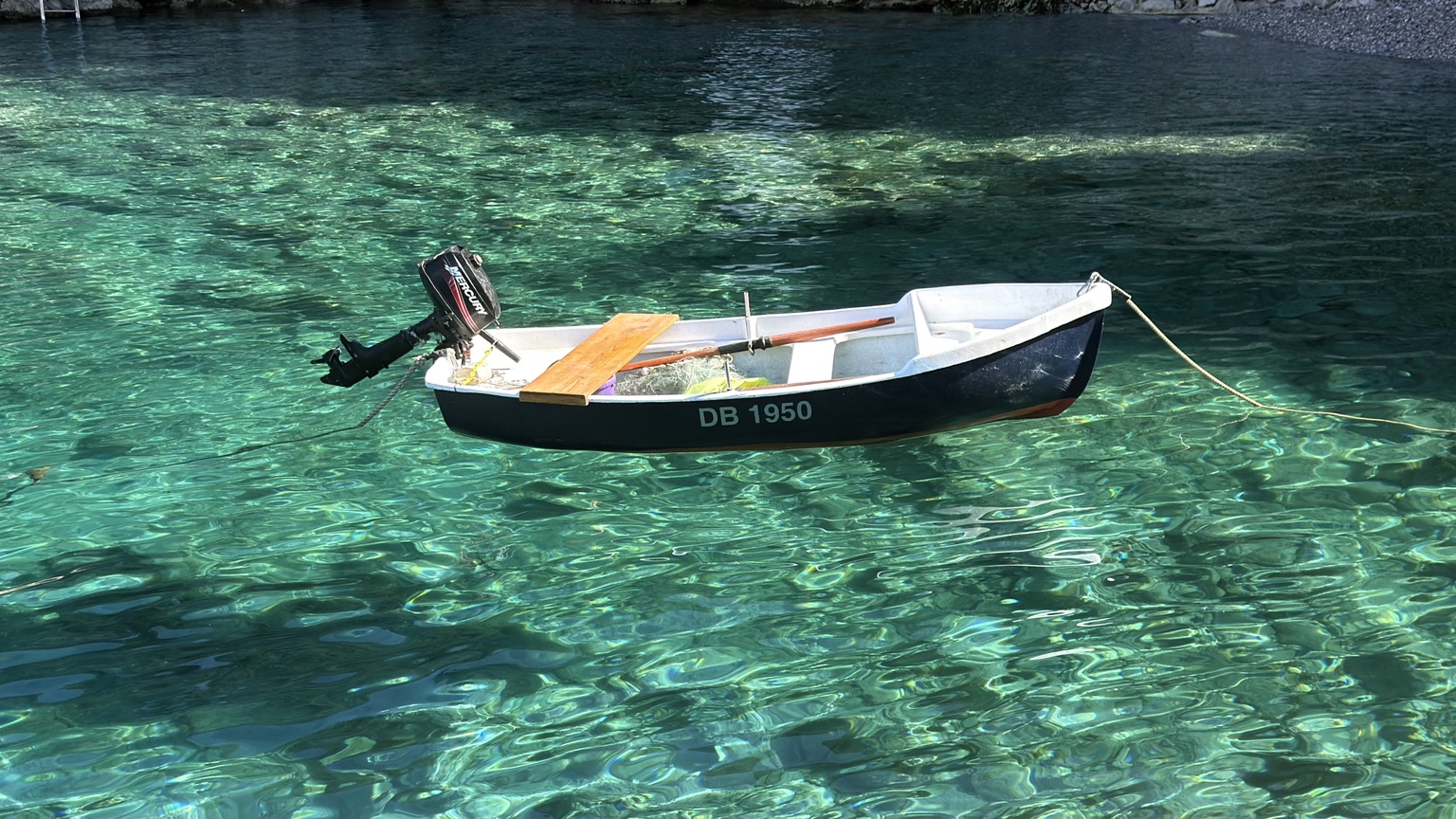 A small black and white fishing boat floating over clear turquoise water