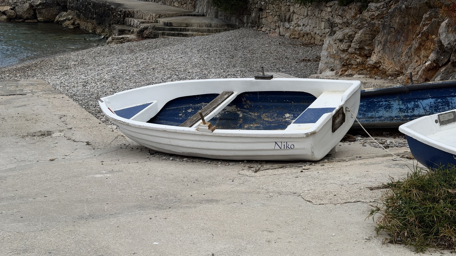 A small white rowing boat named Niko pulled onto a pebble beach