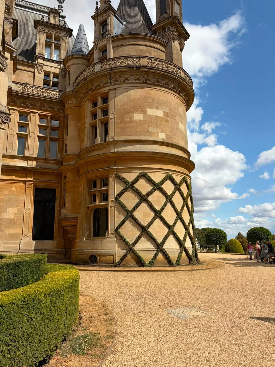 The ornate golden-stone towers and curved façade of Waddesdon Manor beneath a bright blue sky