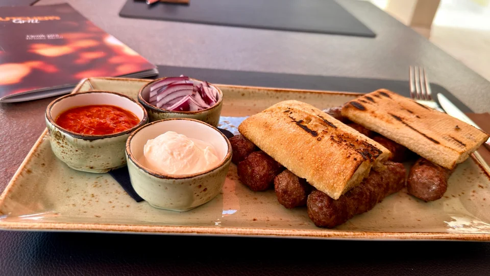 A plate of ćevapi with grilled bread, ajvar, onions and cream