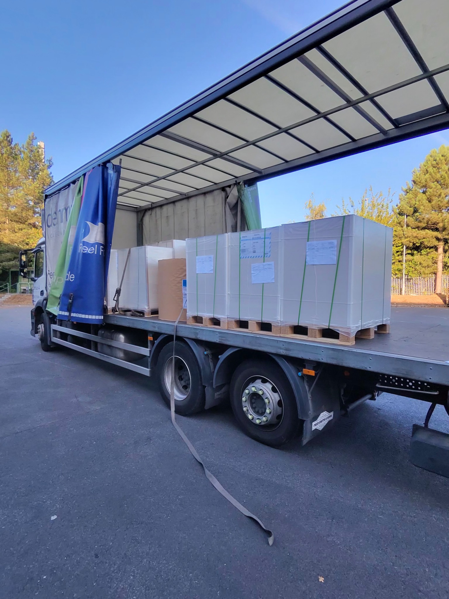 Wrapped pallets of paper secured on the open bed of a curtainside rigid truck