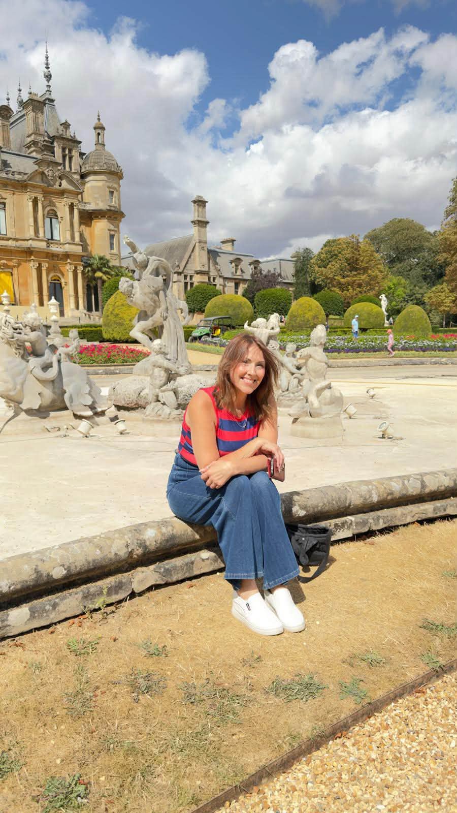 Fiona smiling beside the ornate fountain with Waddesdon Manor and its formal gardens behind her