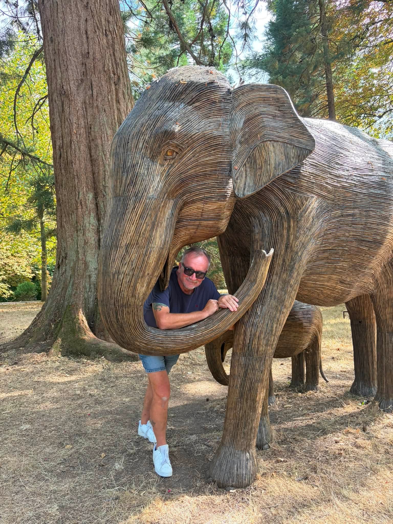 John leaning through the curved trunk of a large woven elephant sculpture