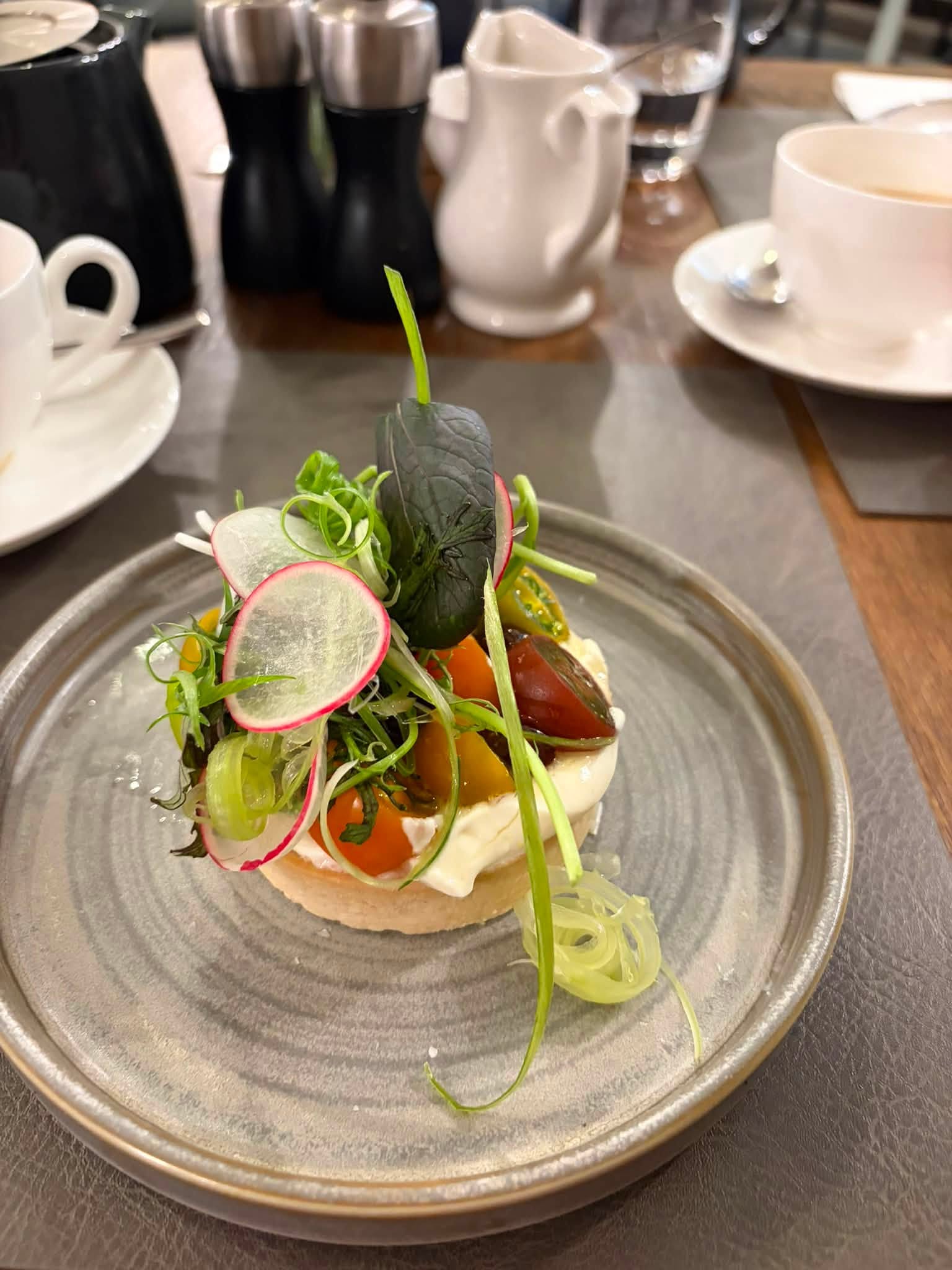 A beautifully presented tomato tart with soft cheese, radish, leaves and herbs