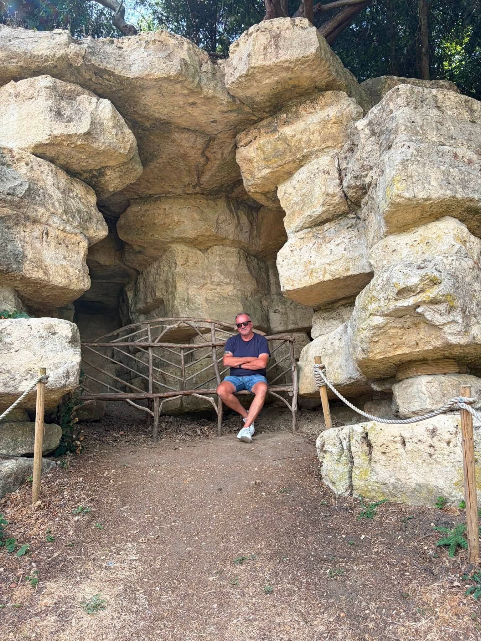 John sitting on a rustic bench inside a monumental rocky grotto at Waddesdon Manor